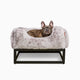 Frenchie in Light grey faux fur elevated dog beds by Fuzi, designed for enhanced airflow, support, and comfort, in light grey fur with a black metal base.