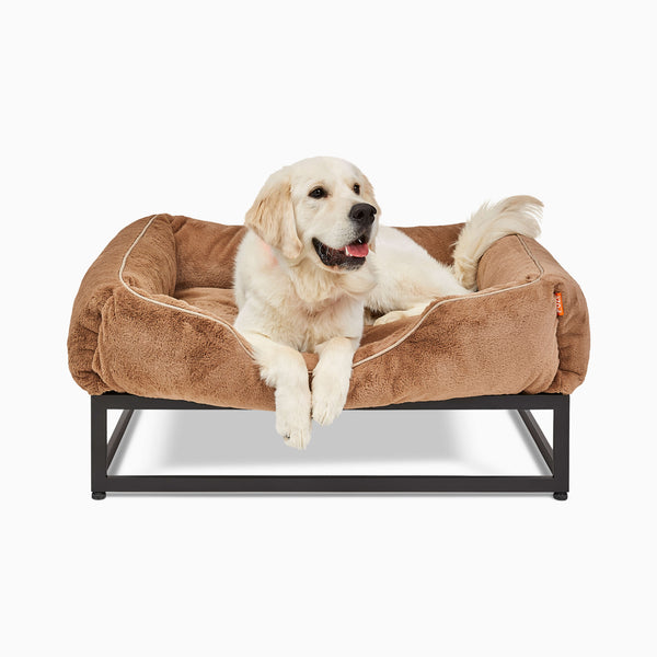 White large dog in a light brown faux fur elevated dog bed for large dogs by Fuzi, designed for enhanced airflow, support, and comfort, in light brown plush with a black metal base.